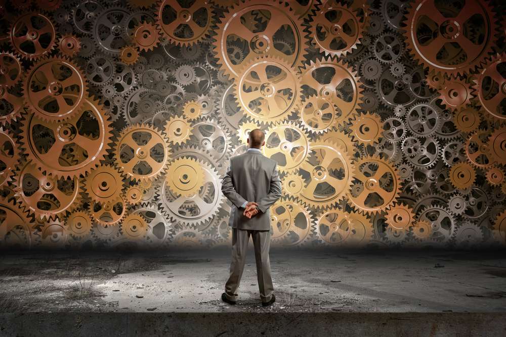 Back view of businessman looking at mechanism of cogwheels Back view of businessman looking at mechanism of cogwheels